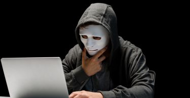 Trolling. Man in mask looking at a monitor. Hacking. Internet. Thinking.