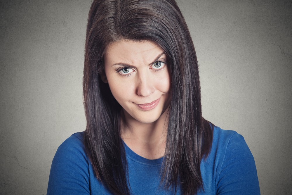 Closeup portrait headshot skeptical young woman looking suspicious with some disgust on her face, mixed with disapproval, isolated grey background. Negative human emotion facial expression feeling